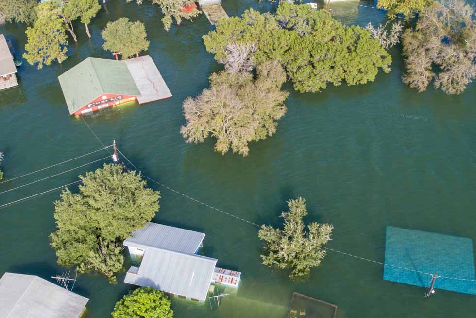 An overhead shot showing several houses and trees partially submerged in dark floodwaters.